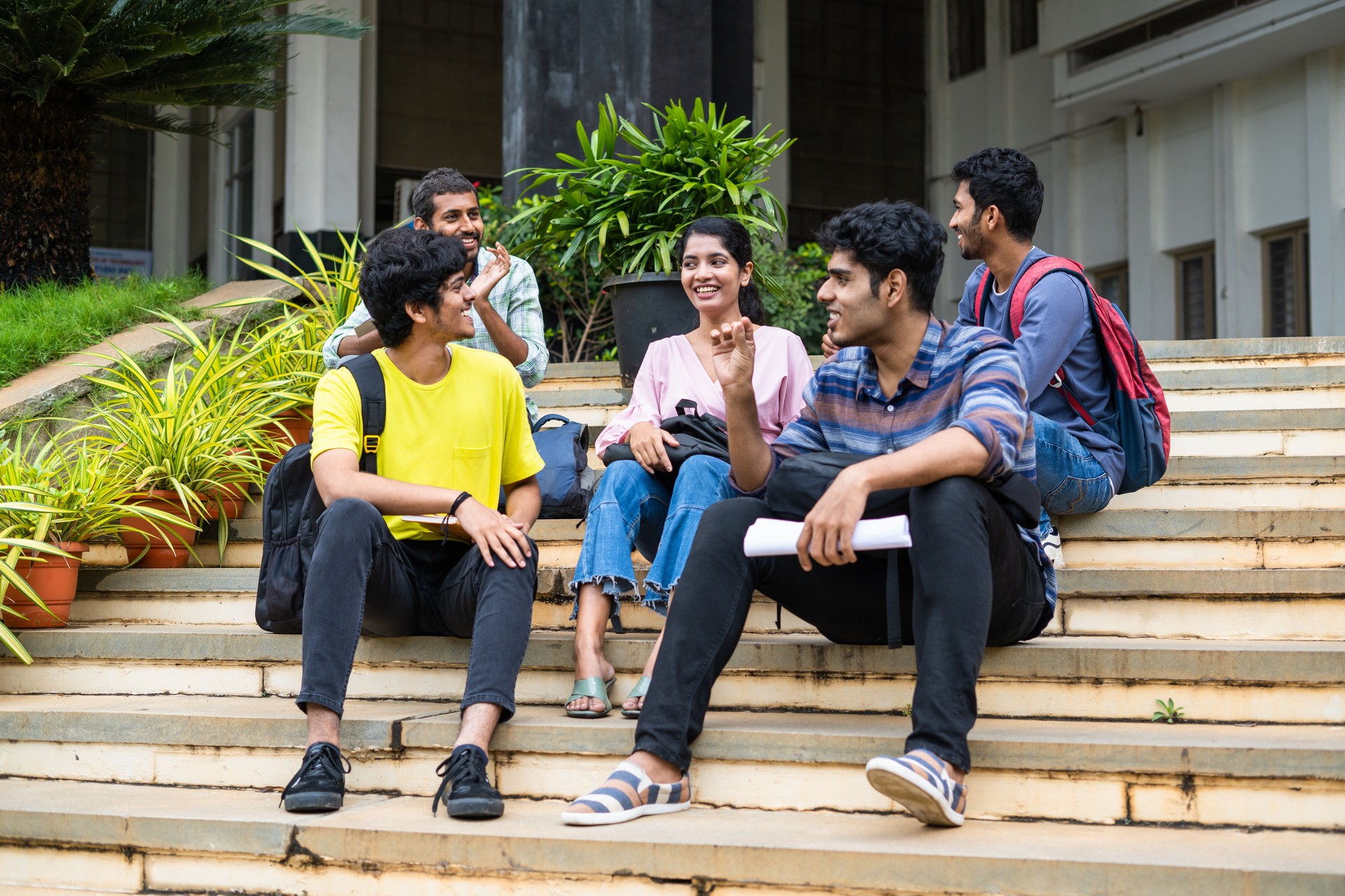 Group of happy students having chat with talking each other while sitting on college campus - concept of friendship, break time and communication